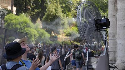 Tourists cool off near a fan as they queue to enter Rome's Colosseum.