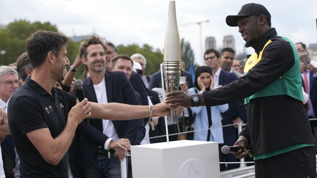 Paris 2024 Olympics Organizing Committee President Tony Estanguet, left, passes the Olympic torch to former Jamaican athlete Usain Bolt,Tuesday, July 25, 2023 in Paris. 