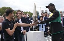 Paris 2024 Olympics Organizing Committee President Tony Estanguet, left, passes the Olympic torch to former Jamaican athlete Usain Bolt,Tuesday, July 25, 2023 in Paris.