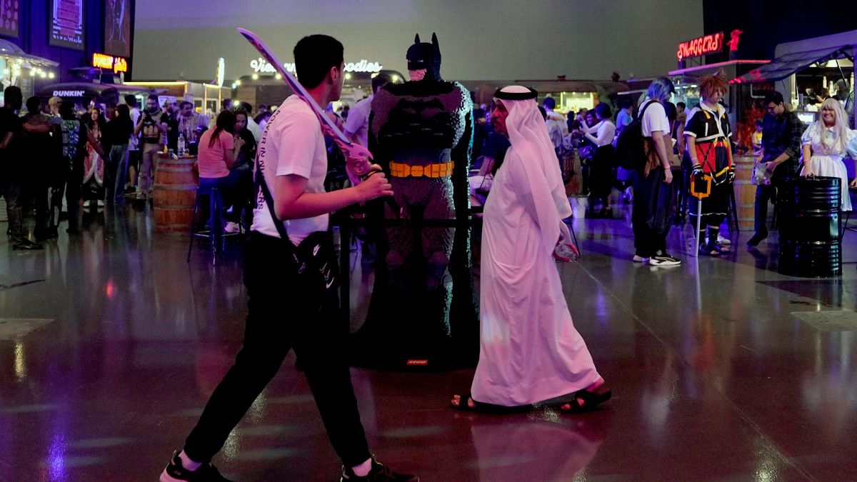 یک مرد اماراتی در جریان جشنواره بازی‌های ورزش الکترونیکی در دبی، امارات متحده عربی، شنبه، ۲۴ ژوئن ۲۰۲۳، از کنار یک شخصیت بتمن عبور می‌کند. 