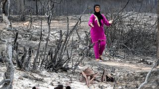 Uma mulher caminha pelas cinzas do incêndio de Melloula, na Tunísia, perto da Argélia