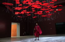A man wearing traditional Masai clothes walks under an installation, at the Biennale International Architecture exhibition, in Venice, Italy, Wednesday, May 17, 2023. 