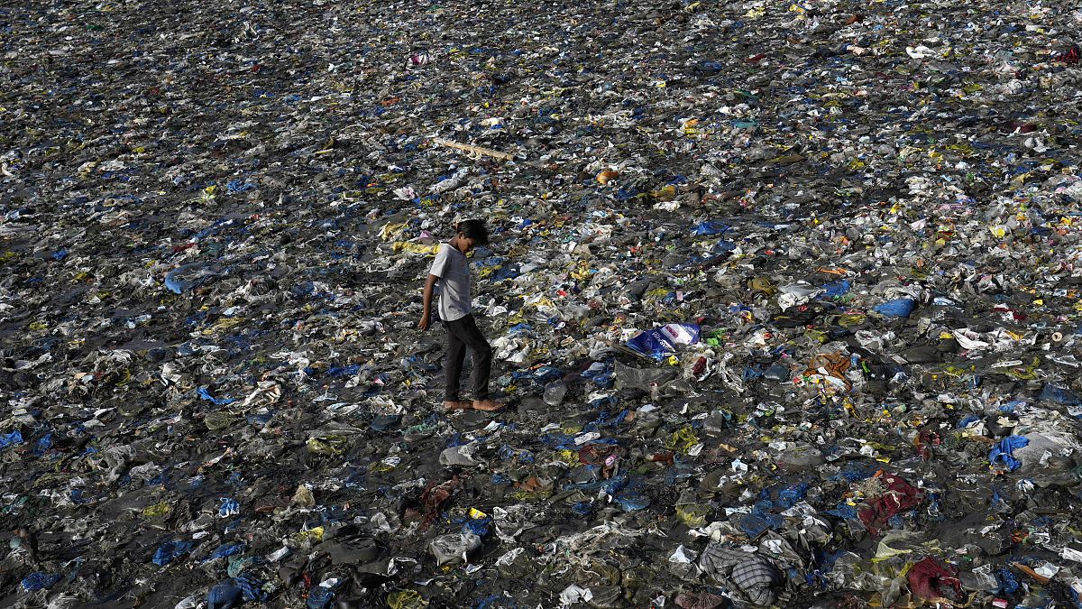 Um rapaz caminha sobre os resíduos de plástico na praia de Badhwar Park, na costa do Mar Arábico, em Bombaim, na Índia,