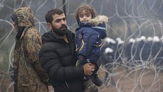 A migrant with a child walks along the barbed wire fence as other gather at the Belarus-Poland border near Grodno, Belarus, Nov. 14, 2021.