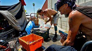 Two men pour ice into a bucket in "The Zone" homeless encampment in Phoenix, Arizona.