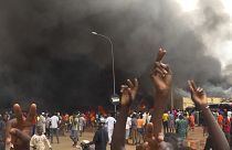 With the headquarters of the ruling party burning in the back, supporters of mutinous soldiers demonstrate in Niamey, Niger, Thursday, July 27 2023.
