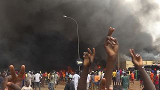 With the headquarters of the ruling party burning in the back, supporters of mutinous soldiers demonstrate in Niamey, Niger, Thursday, July 27 2023. 
