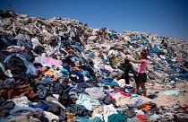 Una donna cerca vestiti usati tra le tonnellate scartate nel deserto di Atacama, Cile