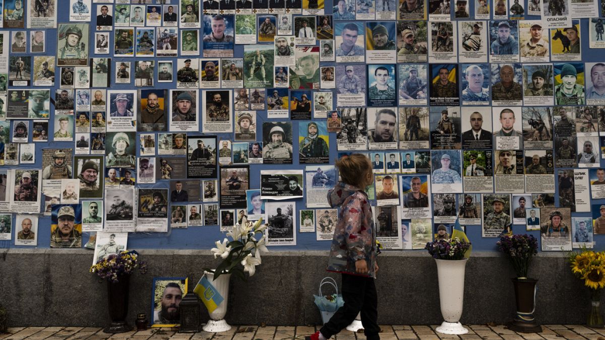 Kislány az elesett ukrán katonák fotói előtt Kijevben 2023. július 27-én