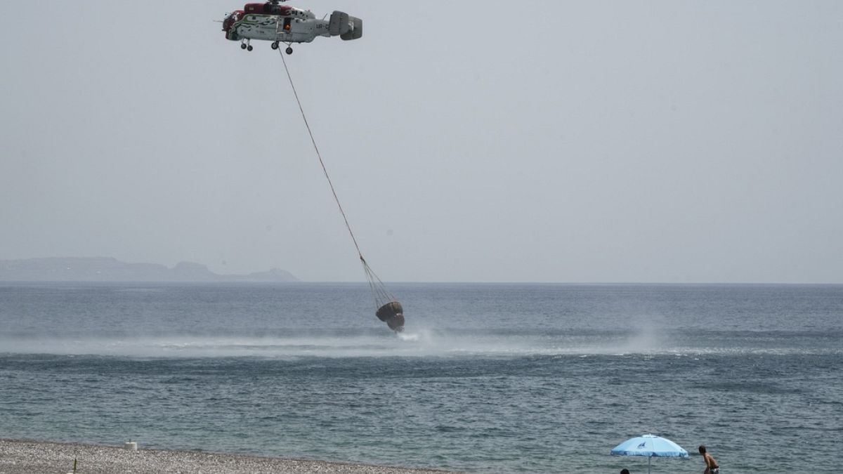 Beachgoers watch a helicopter filling water from the sea during a wildfire, near Gennadi village, on the Aegean Sea island of Rhodes, southeastern Greece, on July 27, 2023. 