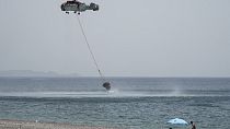 Beachgoers watch a helicopter filling water from the sea during a wildfire, near Gennadi village, on the Aegean Sea island of Rhodes, southeastern Greece, on July 27, 2023.