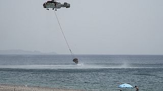 Beachgoers watch a helicopter filling water from the sea during a wildfire, near Gennadi village, on the Aegean Sea island of Rhodes, southeastern Greece, on July 27, 2023. 