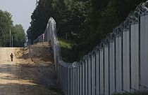 A Polish border guard patrols the area of a built metal wall on the border between Poland and Belarus, near Kuznice, Poland, on June 30, 2022.