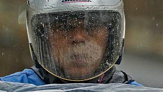 Rainwaters is seen on a windshield of a rider's helmet as he wades through a street in Beijing, Tuesday, Aug. 1, 2023.