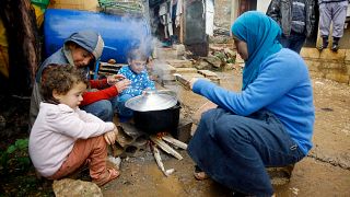 لاجئون سوريون في لبنان يجتمعون حول موقدة وعليها إناء يطبخون في الأكل