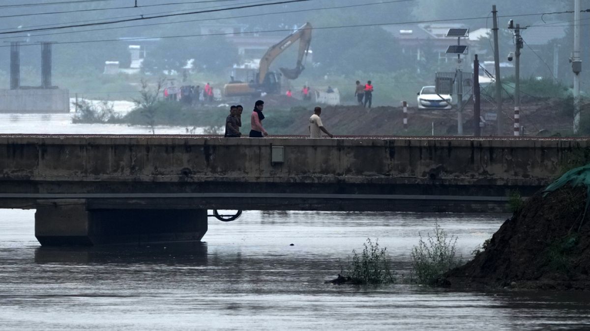 Люди идут по закрытому мосту, частично затопленному разлившейся рекой / Провинция Хэбэй, Китай.