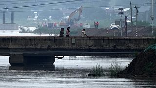 People walk through a closed bridge, partially submerged by a swollen river as workers were using machinery to block the floodwater at a village in the Hebei province, China.