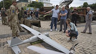 Varias personas observan los drones rusos instalados como símbolo de guerra en el centro de Kiev, Ucrania, el jueves 15 de junio de 2023.