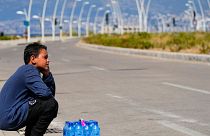 A young street vendor sits next to a pack of water bottles as he waits for customers during a sweltering day on the Mediterranean Sea corniche in Beirut, Lebanon