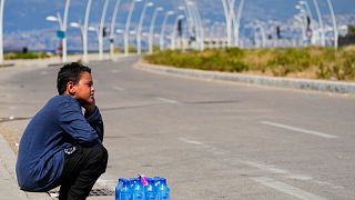 A young street vendor sits next to a pack of water bottles as he waits for customers during a sweltering day on the Mediterranean Sea corniche in Beirut, Lebanon