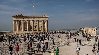 Turisti visitano la collina dell'Acropoli con il tempio del Partenone, vecchio di 2.500 anni, a sinistra, e l'antico tempio dell'Eretteo, a destra, ad Atene, in Grecia, l'11 ottobre 2022.