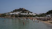 Touristen genießen den Strand und das Meer in Lindos, auf der Ägäisinsel Rhodos im Südosten Griechenlands.