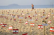 A man runs past Lebanese flags placed in honor of those who died in the 2020 Beirut port explosion on the third anniversary of the blast, on Copacabana beach in Rio de Janeiro
