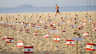A man runs past Lebanese flags placed in honor of those who died in the 2020 Beirut port explosion on the third anniversary of the blast, on Copacabana beach in Rio de Janeiro
