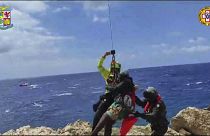 صورة مأخوذة من مقطع فيديو وزعته فرق إنقاذ جبال الألب الإيطالية يوم الأحد 6 أغسطس 2023 لمهاجر تقطعت به السبل على شعاب صخرية في جزيرة لامبيدوسا الإيطالية