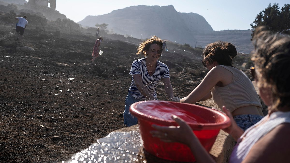 Turistas alemanes junto con residentes intentan extinguir un incendio, cerca de la localidad de Lindos, en la isla de Rodas, al sureste de Grecia, el 24 de julio de 2023.