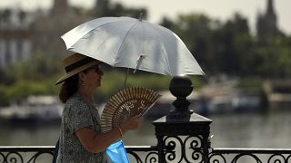امرأة تستخدم مظلة ومروحة لحماية نفسها من أشعة الشمس ودرجات الحرارة المرتفعة في إشبيلية، إسبانيا، في 7 أغسطس 2023.