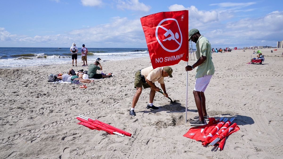 عمال إدارة الحدائق والاستجمام بمدينة نيويورك يضعون علمًا أحمر يحذر الزوار من السباحة على شاطئ روكواي بعد حادثة القرش، الثلاثاء 8 أغسطس 2023، في حي كوينز في نيويورك.