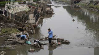 سكان يغسلون حقائبهم وممتلكاتهم على الضفة المتضررة لقناة مسدودة بحطام الفيضانات في أعقاب مياه الفيضانات
