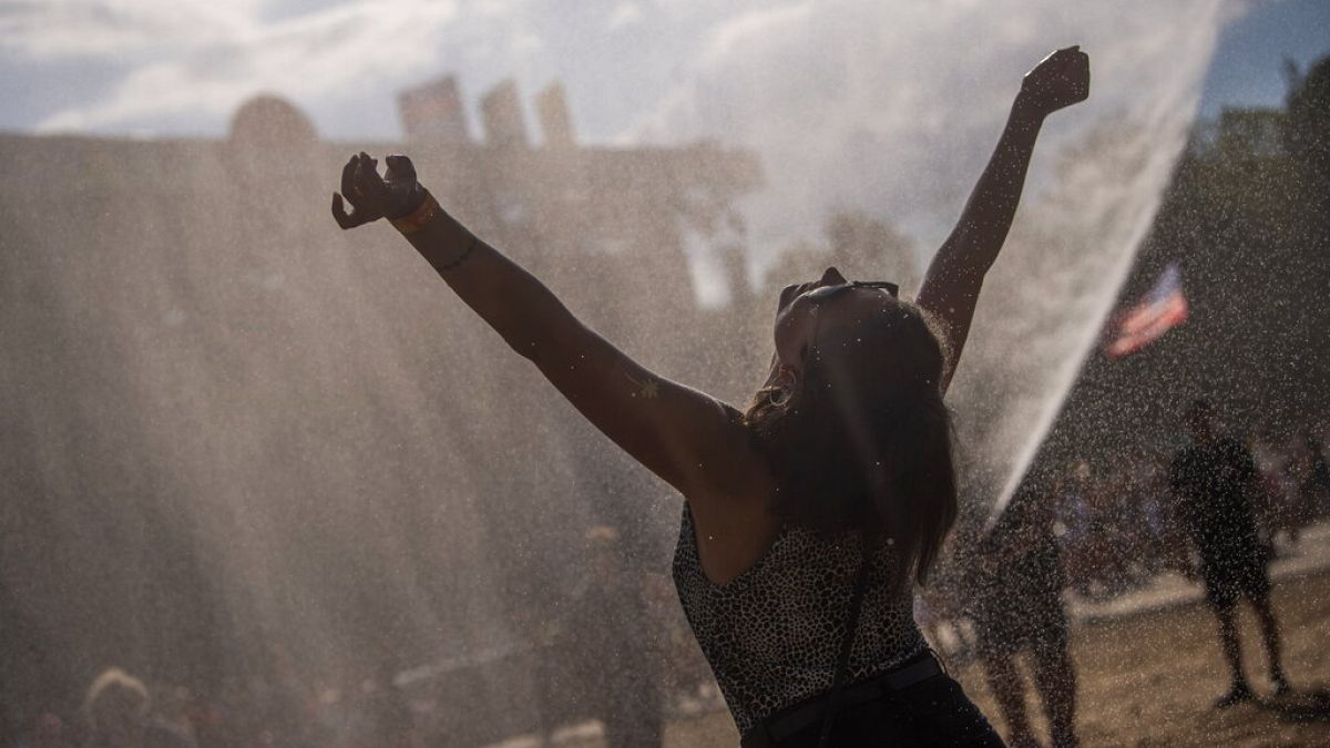 Eine junge Frau genießt im Sonnenschein Wassertropfen, die aus einem Schlauch gesprüht werden.