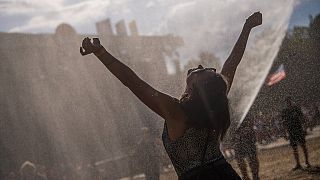 Eine junge Frau genießt im Sonnenschein Wassertropfen, die aus einem Schlauch gesprüht werden.