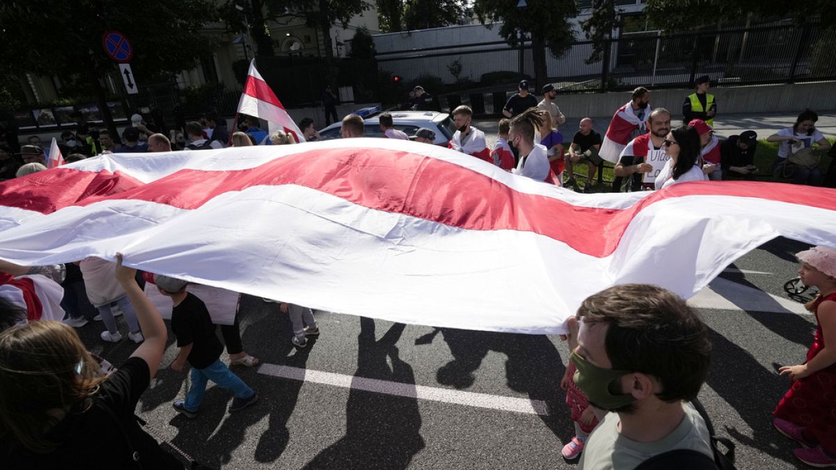 FILE - Protesters carrying the white-and-red banner of the Belarusian opposition march past the U.S. Embassy in Warsaw, Poland, on Sunday, Aug. 8, 2021. 