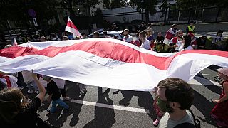 FILE - Protesters carrying the white-and-red banner of the Belarusian opposition march past the U.S. Embassy in Warsaw, Poland, on Sunday, Aug. 8, 2021.