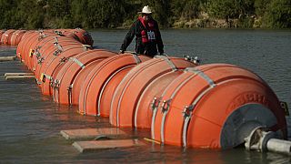 A kayaker walks past large buoys being used as a floating border barrier on the Rio Grande Tuesday