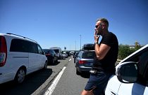 Um turista alemão fuma um cigarro junto ao carro enquanto espera numa fila de quilómetros à entrada da autoestrada que conduz ao Mar Adriático,