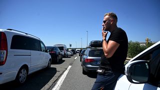 Um turista alemão fuma um cigarro junto ao carro enquanto espera numa fila de quilómetros à entrada da autoestrada que conduz ao Mar Adriático, 