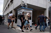 Adeptos de futebol, na sua maioria croatas, cobrem a cara enquanto a polícia os escolta da Direção-Geral da Polícia de Ática para o tribunal, em Atenas, Grécia, no domingo, 13 de agosto,