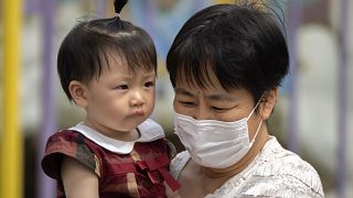 Archivo: una mujer con mascarilla lleva en brazos a un niño mientras pasean por un parque público de Pekín, el 1 de junio de 2023.