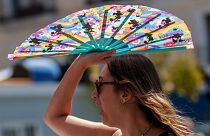 Uma mulher protege-se do sol com uma ventoinha de mão em Madrid, Espanha, em julho de 2023\.