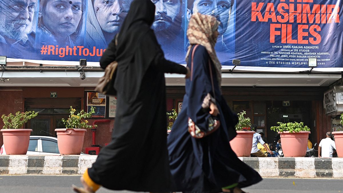 نساء تسرن أمام لافتة من فيلم بوليوود "ملفات كشمير"