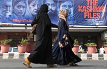 نساء تسرن أمام لافتة من فيلم بوليوود "ملفات كشمير"