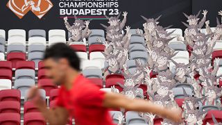 Ein Athlet läuft im Stadion vorbei an den offiziellen Maskottchen der diesjährigen Leichtathletik-WM in Budapest