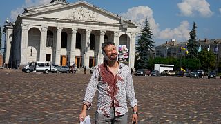 An injured man walks in Krasna square with the theatre in the background, after a Russian attack, Saturday, Aug. 19, 2023. in Chernihiv, Uk