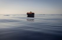 People equipped with life jackets set sail in a wooden boat in the Mediterranean Sea.