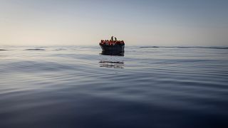 People equipped with life jackets set sail in a wooden boat in the Mediterranean Sea.