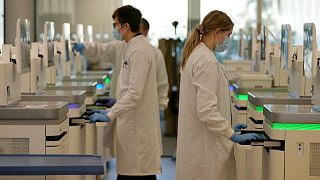 Investigadores observam as máquinas de sequenciação que analisam o material genético de casos de COVID-19, em Inglaterra